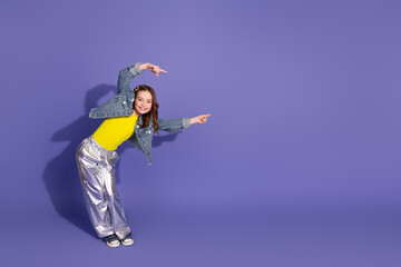 Young stylish girl in vibrant outfit striking a cheerful pose against a purple studio background...