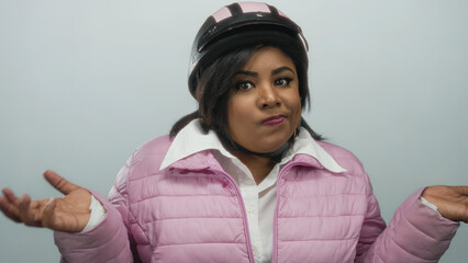 Woman gesturing in frustration wearing a pink jacket and helmet against a white background, conveying uncertainty and expressing a questioning attitude in a stock photo.