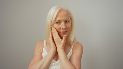 Woman with albinism gently touching her face, standing on an isolated white background, exhibiting...