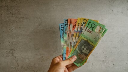 Hand holding australian dollar banknotes against a concrete background, depicting financial...