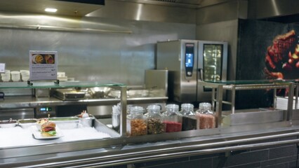 Restaurant kitchen with defocused bokeh background showing blurred jars and a food counter with various ingredients in a professional cooking environment.