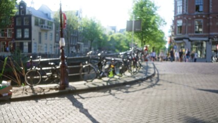 Blurred view of bicycles parked along a sunlit amsterdam canal with historic buildings and leafy trees in the background, creating a dreamy urban scene. © Krakenimages.com