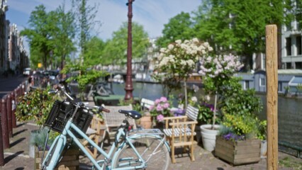 Amsterdam scene with blurred bicycle and flowers near canal, showcasing defocused urban setting with greenery and iconic netherlands canal view.