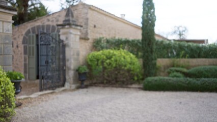 Fototapeta na wymiar Blurred view of a mediterranean garden featuring an old stone wall and a wrought iron gate surrounded by lush greenery, creating a tranquil and timeless atmosphere.