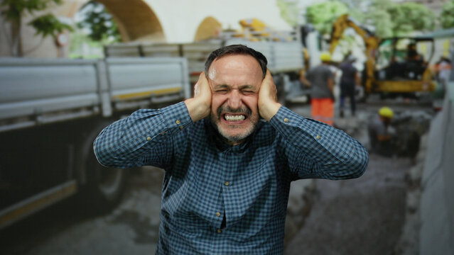 Man covering ears and screaming at a noisy construction site where workers in helmets operate machinery creating a chaotic and stressful atmosphere indicative of urban life.