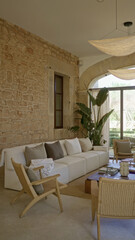 Modern living room indoors with elegant furniture and mediterranean stone wall in bright open house featuring plants and comfortable seating.