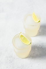 Refreshing lime cocktails on white table. Glass of citrus hard seltzer with ice cube and fresh lime...