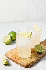 Refreshing lime cocktails on wooden board. Two glasses of citrus hard seltzer with ice cube and fresh lime slices. Summer lemonade, mocktail, vitamin water concept. Daiquiri, gimlet, margarita.