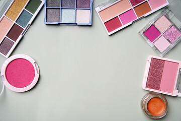 Makeup palettes and blush forming a frame on a pastel green background