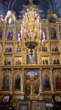 Capriana Monastery indoors view of traditional ornate Christian Orthodox church located in Moldova. Scene during divine service with a monk praying at the altar underneath a grand gilded chandelier