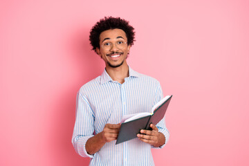Confident young professional reading a book while smiling on vibrant pink background in casual...