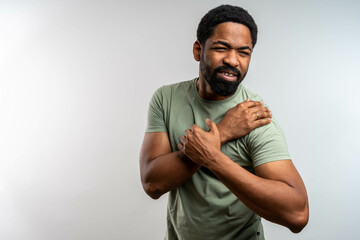 Handsome young Black man in green t-shirt over isolated grey background suffering from pain in...