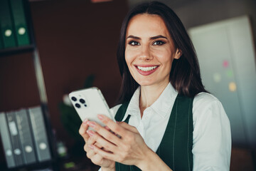 Confident professional businesswoman holding a smartphone in an office environment, showcasing...