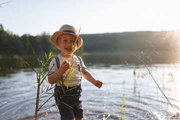 Toddler walking through lake shallows in rubber boots
