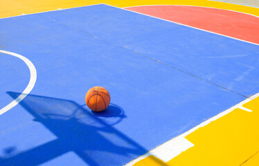 Basketball on outdoor basketball court with colorful outline pattern on concrete yard floor surface...