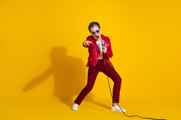 Confident Elderly Woman Singing in a Glamorous Red Outfit Against Vibrant Yellow Background with Microphone