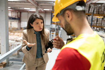 The manager expresses concerns to a safety officer during a warehouse meeting, focusing on safety standards and procedures.