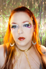 Fototapeta premium A vibrant and artistic portrait of a woman with striking red hair and bold, colorful makeup. Her eye makeup features a rainbow gradient with rhinestones and dramatic false lashes.