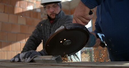 Angle grinder cutting metal, sparks flying as two workers focus on precision and safety, one holding metal steady, collaborative metalworking task, 800 fps slow motion