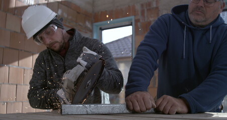Angle grinder sparks during metal cutting, workers in protective gear collaborating on construction...