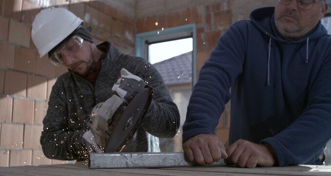 Angle grinder sparks during metal cutting, workers in protective gear collaborating on construction task, industrial site in super slow motion
