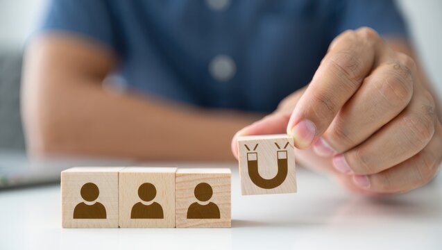 Hand holding magnet icon block attracting people blocks in business concept. Influence, targeting, and human resources in a minimalistic corporate setting.