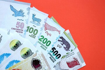 Argentine pesos money bills in big amount lies on red color table close up