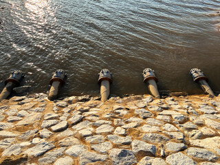 Five drainage pipes lined along a rocky embankment, discharging into a lake under the golden...