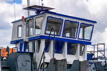 Close-up of a blue and white ship wheelhouse with large windows and technical details against a cloudy sky © Adam