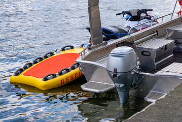 Obraz premium Rescue aluminum boat with outboard engine docked at a pier, featuring a floating yellow and red rescue board on the water