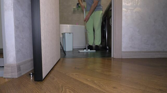 A cleaner man washes in the bathroom in the house. A man washes the floor with a mop in the apartment. Washing with a mop the tiles black. Slow motion.