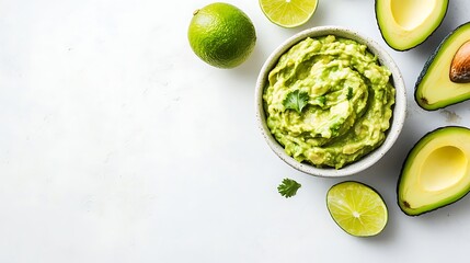Guacamole Bowl with Lime and Avocado Slices on a White Surface. Overhead shot