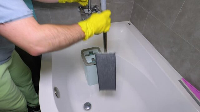 A man fills a bucket with water to wash the floors, a man with a mop in the bathroom. House cleaning. Slow motion