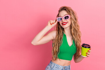 Fashionable young woman wearing stylish summer outfit holding a cup with pink sunglass posing against pink backdrop