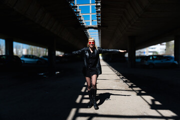Punk style fashion girl in black edgy outfit with leather jacket and bold red sunglasses,...