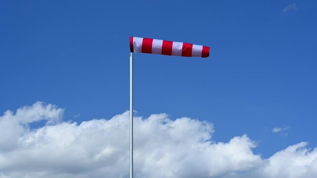 red and white windsock against blue sky and white cumulus clouds