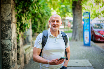 Middle aged man walking on the street and using a smartphone