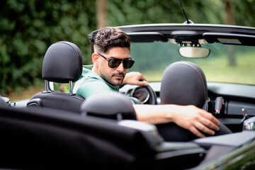 A middle-aged man sitting in a convertible car and driving. Handsome male wearing casual clothes...