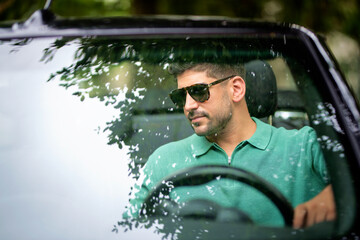 A middle-aged man sitting in a convertible car and driving. Handsome male wearing casual clothes...
