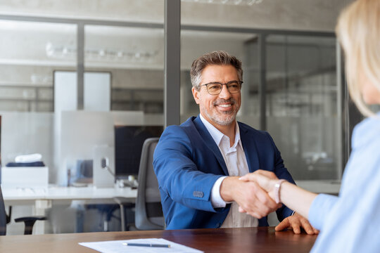 Mature Latino bank worker man shaking hand with client, recruit female employee or business partner after signing a contract. Group of people satisfied with results of team work together. Copy space