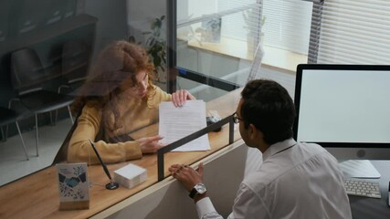 High angle shot of woman with curly red hair getting help with paperwork from bank assistant across counter