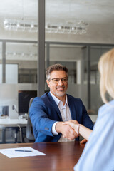 Mature Latino bank worker man shaking hand with client, recruit female employee or business partner...