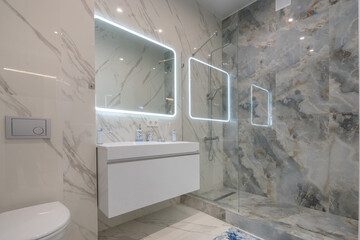 Elegant design of the bathroom, decorated with marble tiles. Illuminated mirror over the sink,...