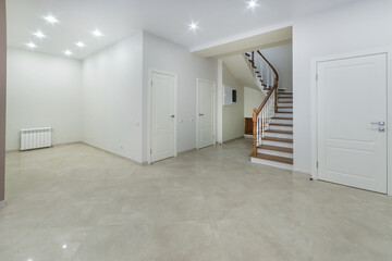 The hall of a country house with white decor of walls and ceiling, beige floor tiles. Stairs with...