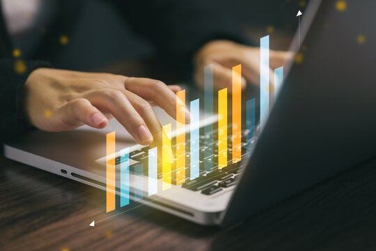 A close-up of a business person typing on a laptop with a digital bar chart overlay, symbolizing data analytics, business growth, and modern financial technology. - Powered by Adobe