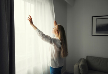 Woman opening window curtains at home in morning