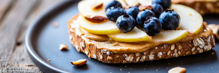A nutritious sandwich features creamy peanut butter spread over whole grain toast, garnished with fresh blueberries and chopped nuts, served on a white plate, banner