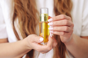 Fototapeta premium Woman holding cosmetic pump bottle. Argan oil or serum product. Golden oil in glass packaging. Hair or skin care. Natural cosmetic in hands. Wellness and beauty item.