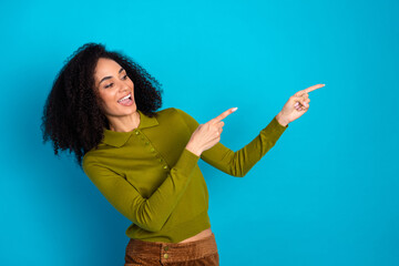 Cheerful young woman in a stylish outfit gesturing and pointing on a bright vibrant blue background.
