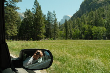 Yosemite National Park in California’s Sierra Nevada mountains green foliage and granite cliffs on a beautiful sunny day with photographer reflection in car mirror